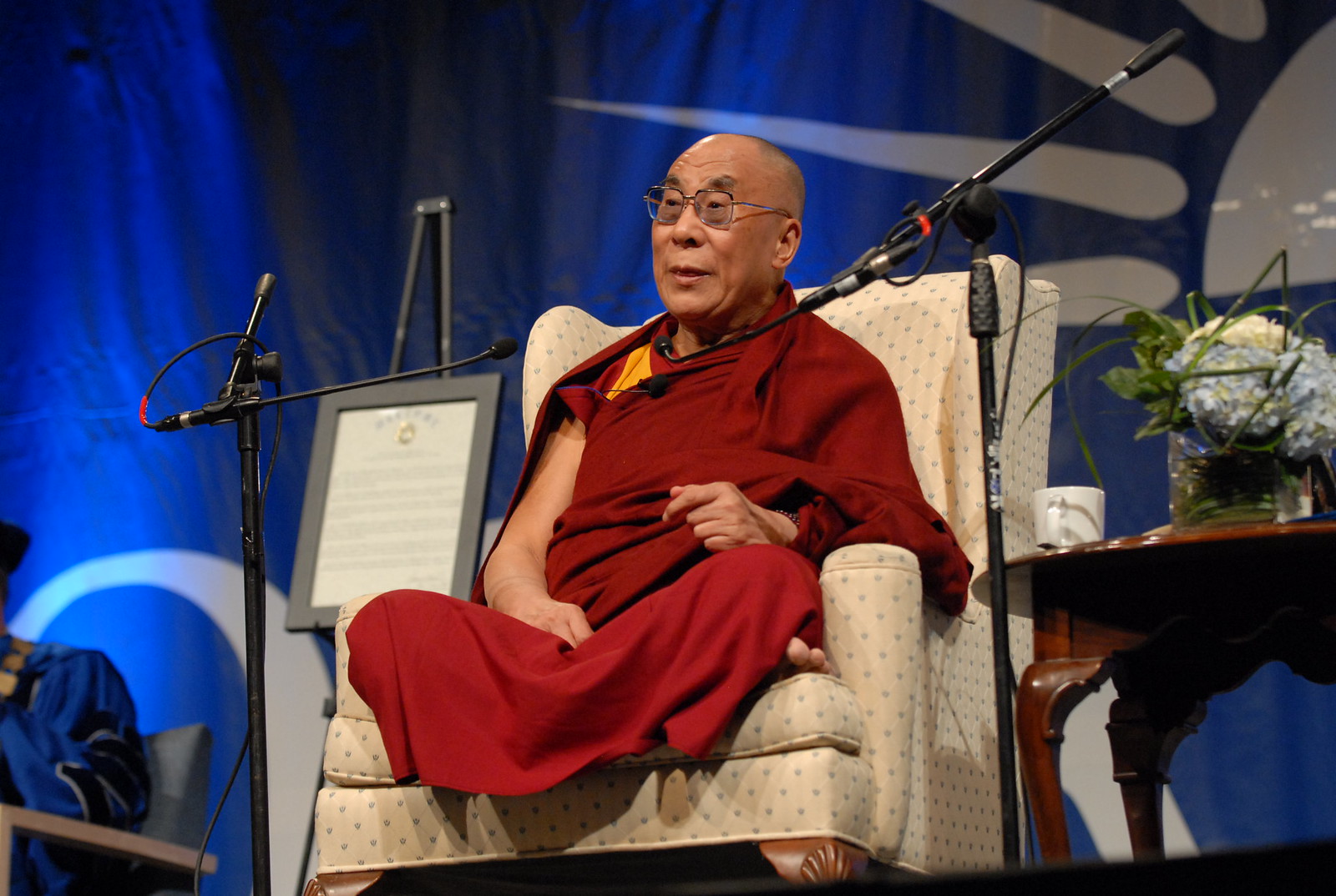 Dalai Lama at NSU. He is seated and is speaking into a microphone.